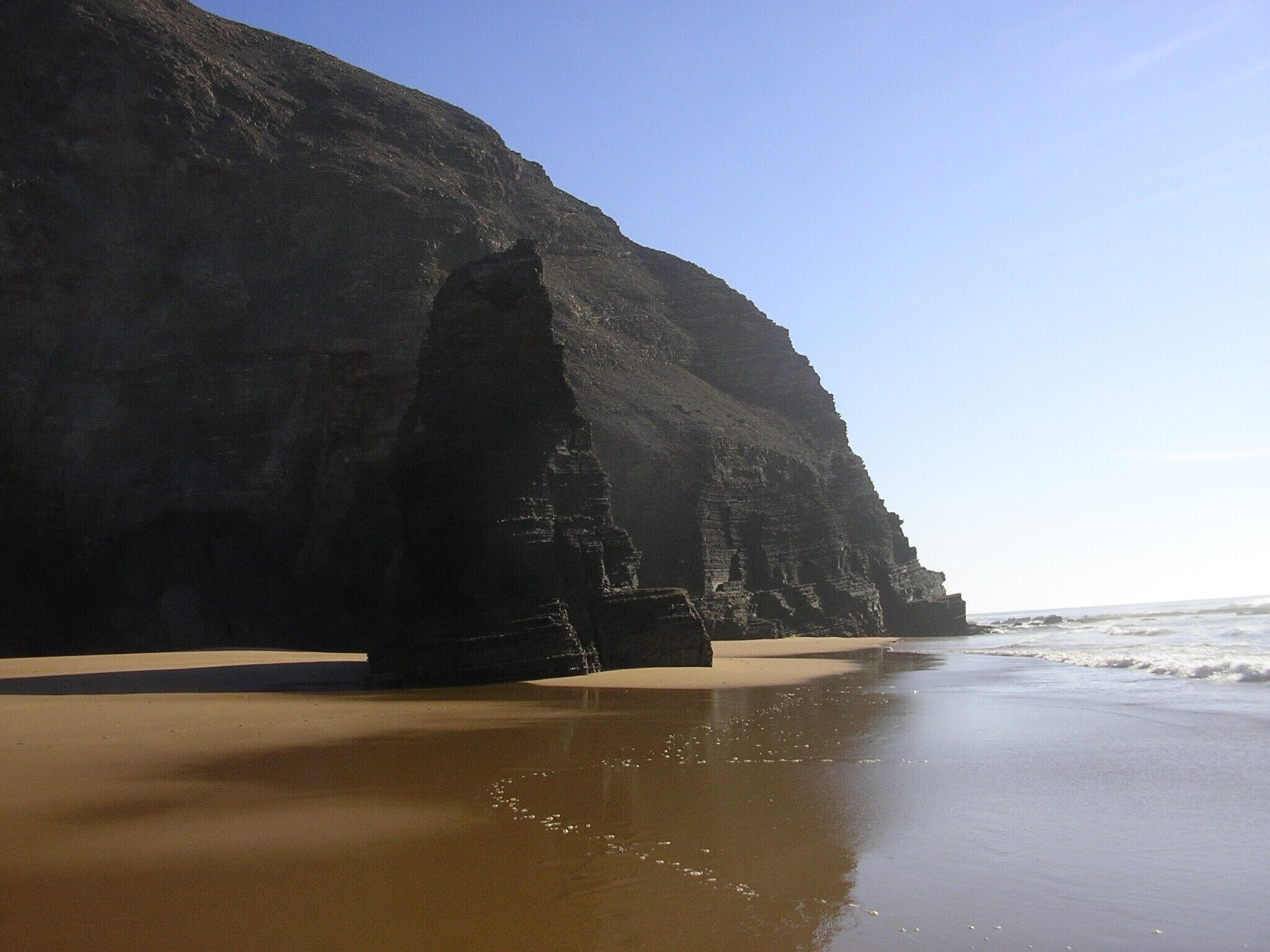 Une plage avec une grande formation rocheuse et des vagues qui se rapprochent du rivage.