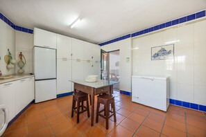 A kitchen with white cabinets, a tiled backsplash, a wooden table with stools, and a refrigerator.