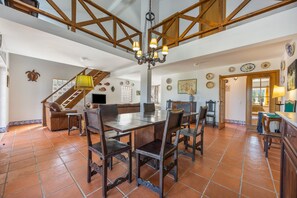 Une salle à manger spacieuse, avec une grande table et des chaises en bois, un lustre et un escalier menant à un niveau supérieur.