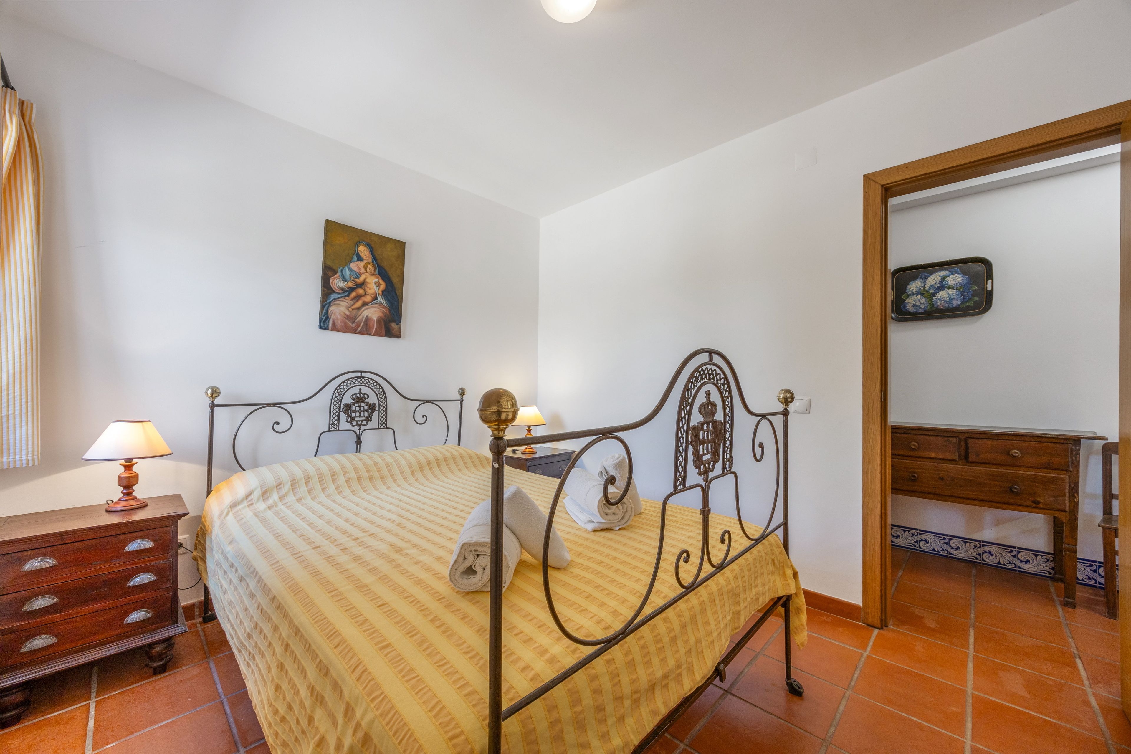 Ein Schlafzimmer mit Bett, Nachttisch, Kommode, einem Gemälde an der Wand und einem Spiegel.