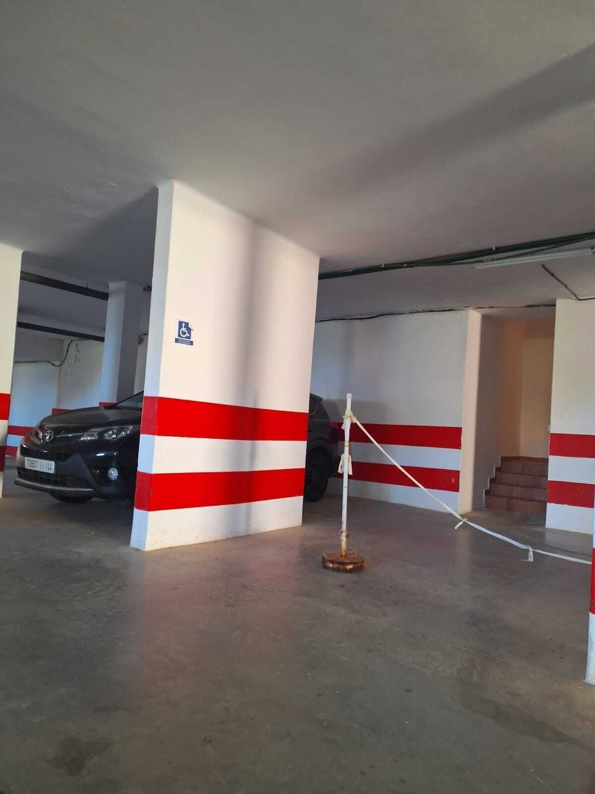 Un estacionamiento con columnas a rayas rojas y blancas, un coche negro estacionado y un cartel de acceso para sillas de ruedas.