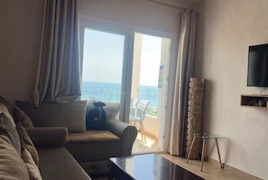 Una habitació d'hotel amb un sofà, una taula petita, un televisor fixat a la paret i vista a l'oceà a través d'una porta corredissa.