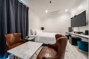 A hotel room with a bed, a desk, a chair, a TV, and a window with curtains.