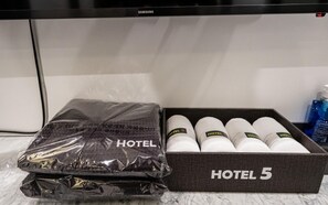 Une boîte noire portant l’inscription « HÔTEL 5 », accompagnée de récipients cylindriques blancs et d’un sac en plastique noir sur lequel est imprimé le mot « HÔTEL ».