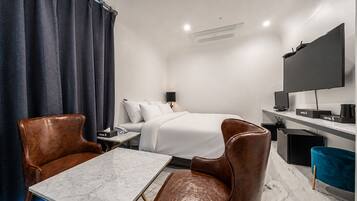 A hotel room with a bed, a desk, a chair, a TV, and a window with curtains.