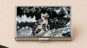 Un objeto metálico con superficie reflectante y un diseño central que presenta una figura estilizada de animal y patrones abstractos.