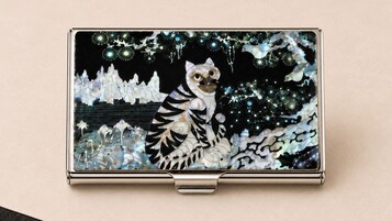 Objeto metálico com superfície refletora e desenho central com animal estilizado e padrões abstratos.