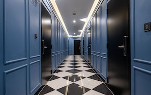 A hotel hallway with blue walls, black and white checkered flooring, and doors on both sides.