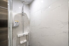A modern bathroom with a shower, marble tiles, and a shelf with toiletries. - Pyeongtaek Hotel 5 (Pyeongtaek)