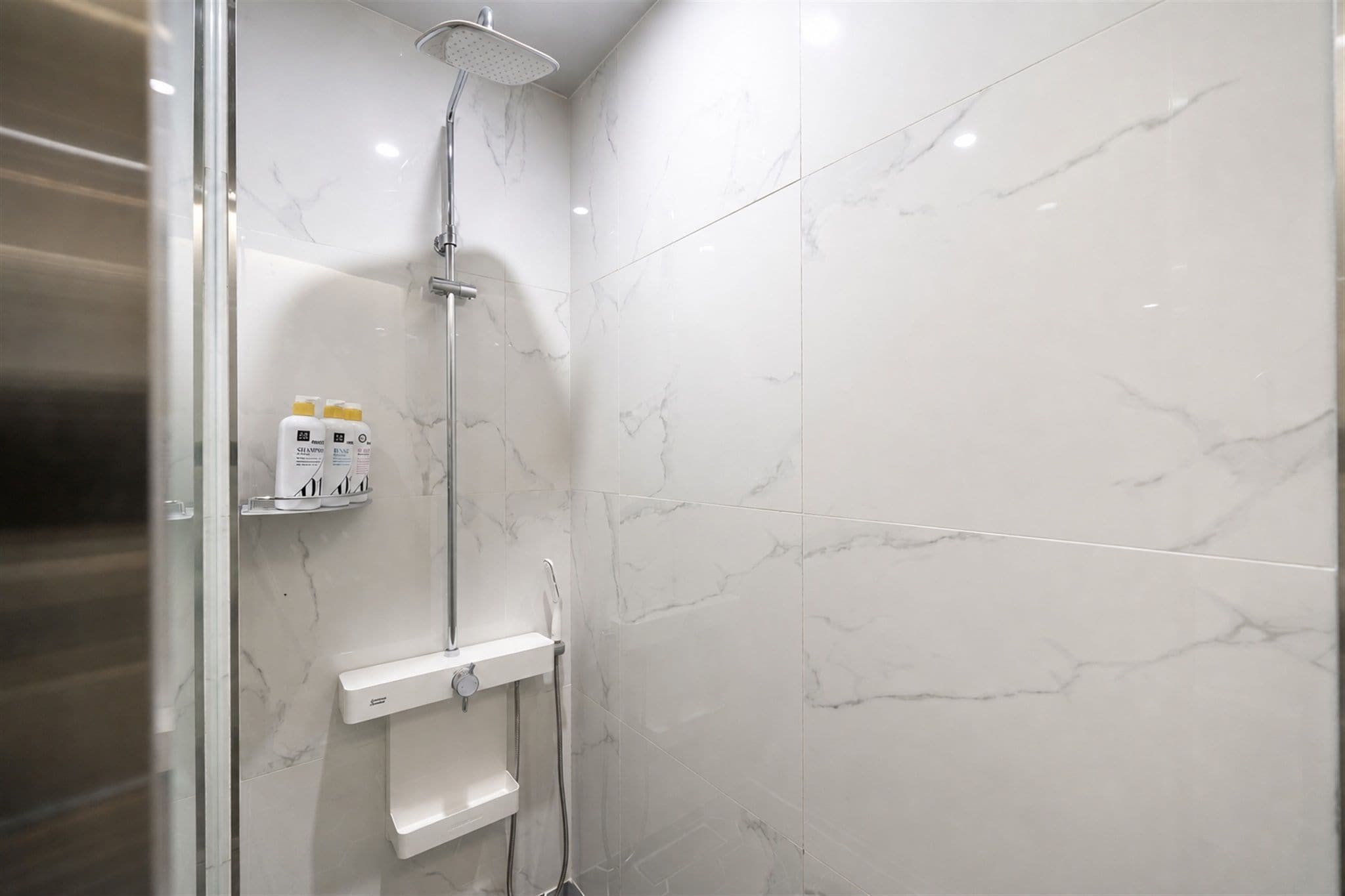 Un baño moderno con ducha, azulejos de mármol y un estante con artículos de aseo.