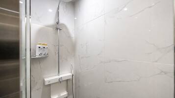 Un baño moderno con ducha, azulejos de mármol y un estante con artículos de aseo.