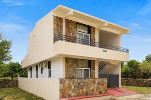 A two-story building with a stone facade, a balcony, and a staircase leading to an upper level. - ELIVAAS Signature Hiara Karma 5BHK Villa (Udaipur)