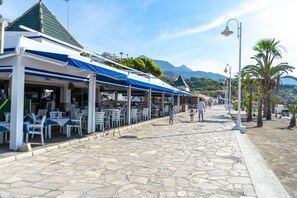 Una calle costera con mesas al aire libre, adoquinado de piedra y palmeras.