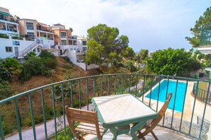 Ein Balkon mit Tisch und Stühlen, der auf einen Pool mit viel Grün und Wohnhäusern blickt.