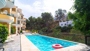 Uma piscina com um boião inflável rosa, rodeada por um deck de pedra e uma cerca de metal.