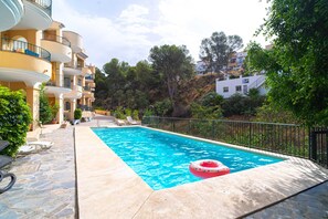 Ein Swimmingpool mit einem rosa Luftring, umgeben von einer Steinterrasse und einem Metallzaun.