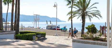 Eine Strandpromenade mit Palmen, Bänken und einem Rettungsturm.