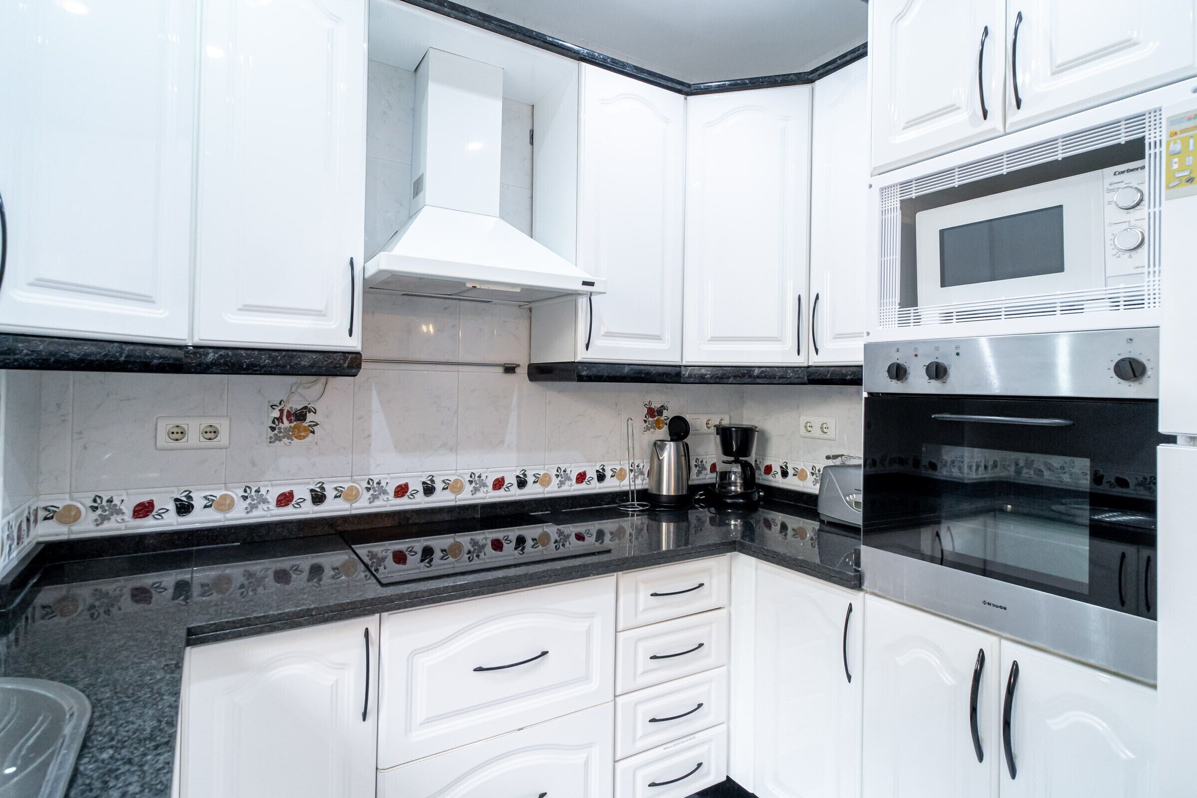 Een moderne keuken met witte kasten, een oven van roestvrij staal en een magnetron.