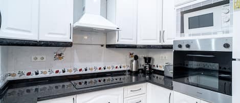 Een moderne keuken met witte kasten, een oven van roestvrij staal en een magnetron.