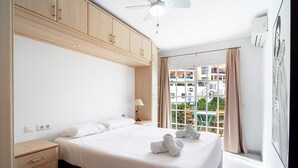 Quarto de hotel com cama, mesa de cabeceira, luminária, ventilador de teto e janela com vista para o exterior.