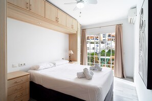 Ein Hotelzimmer mit einem Bett, einem Nachttisch, einer Lampe, einem Deckenventilator und einem Fenster mit Blick nach draußen.