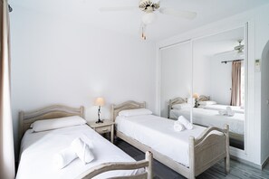 A hotel room with two single beds, a ceiling fan, a bedside table with a lamp, and a large mirror reflecting the room. - Las Flores de Burriana 5 by Casasol (Nerja)