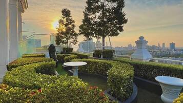 A rooftop garden with manicured hedges, a few trees, and a cityscape in the background.