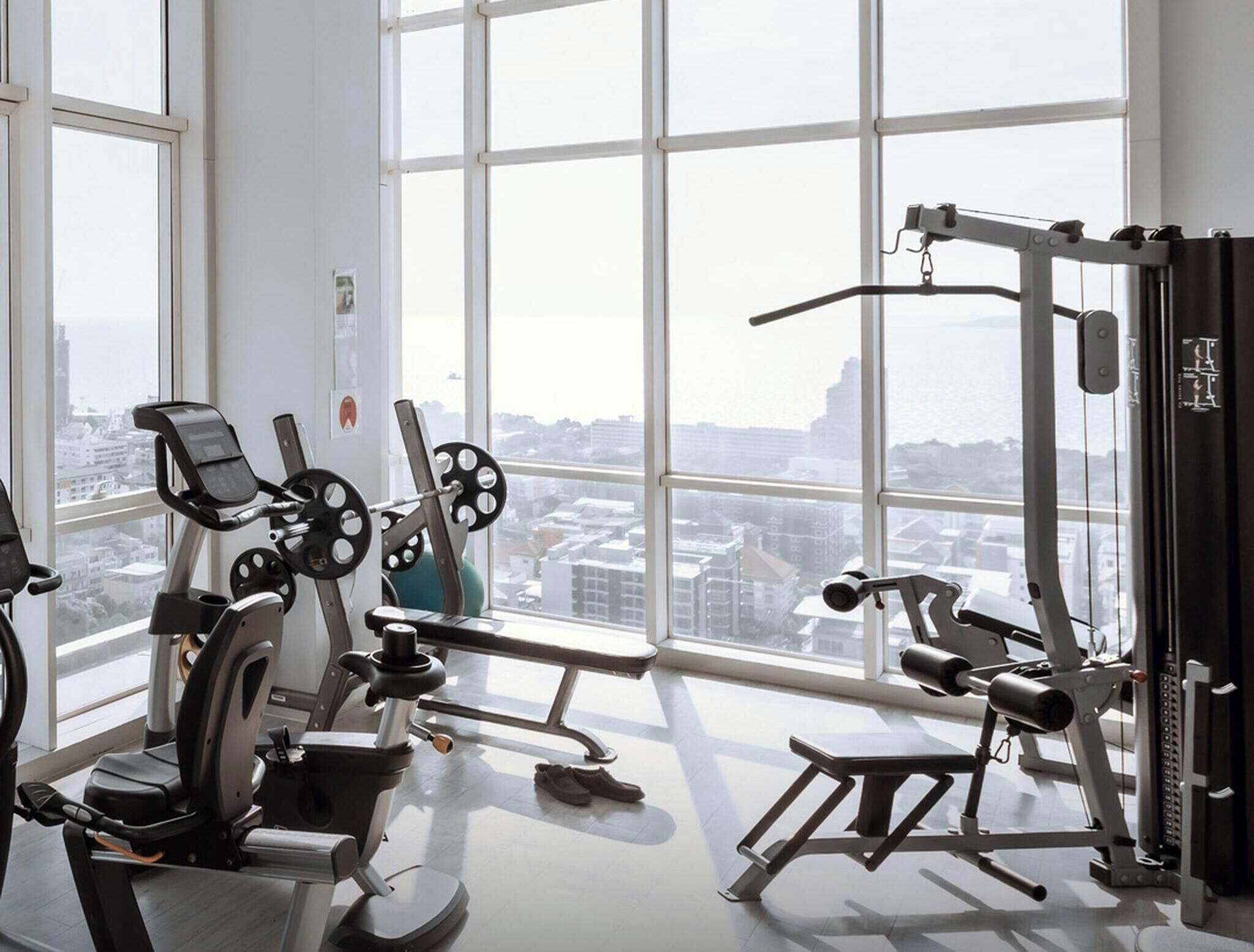 Un gimnasio con equipos de ejercicio variados y ventanas amplias que ofrecen vistas de la ciudad.
