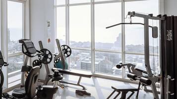 Un gimnasio con equipos de ejercicio variados y ventanas amplias que ofrecen vistas de la ciudad.