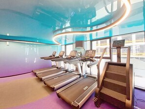 Ein Fitnessstudio mit Laufbändern, Stepper und einem digitalen Bildschirm.