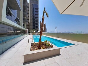 A rooftop pool with a palm tree, surrounded by a glass balustrade and a clear sky. - Airy 1 Bedroom in JVC l Pool & Gym access l near Circle Mall (JVC)