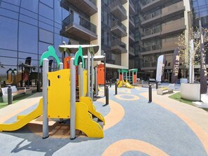 Un espace de jeux extérieur équipé d’appareils de musculation, entouré d’un bâtiment moderne doté de grandes fenêtres.