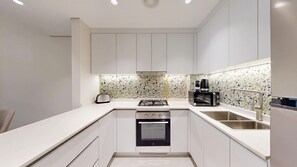 A modern kitchen with white cabinets, a gas stove, a microwave, and a coffee maker. - Airy 1 Bedroom in JVC l Pool & Gym access l near Circle Mall (JVC)