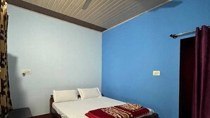 A bedroom with a bed, a ceiling fan, a nightstand, and a door with a curtain. - Honey Drop by Mantra (Chikkamagaluru)