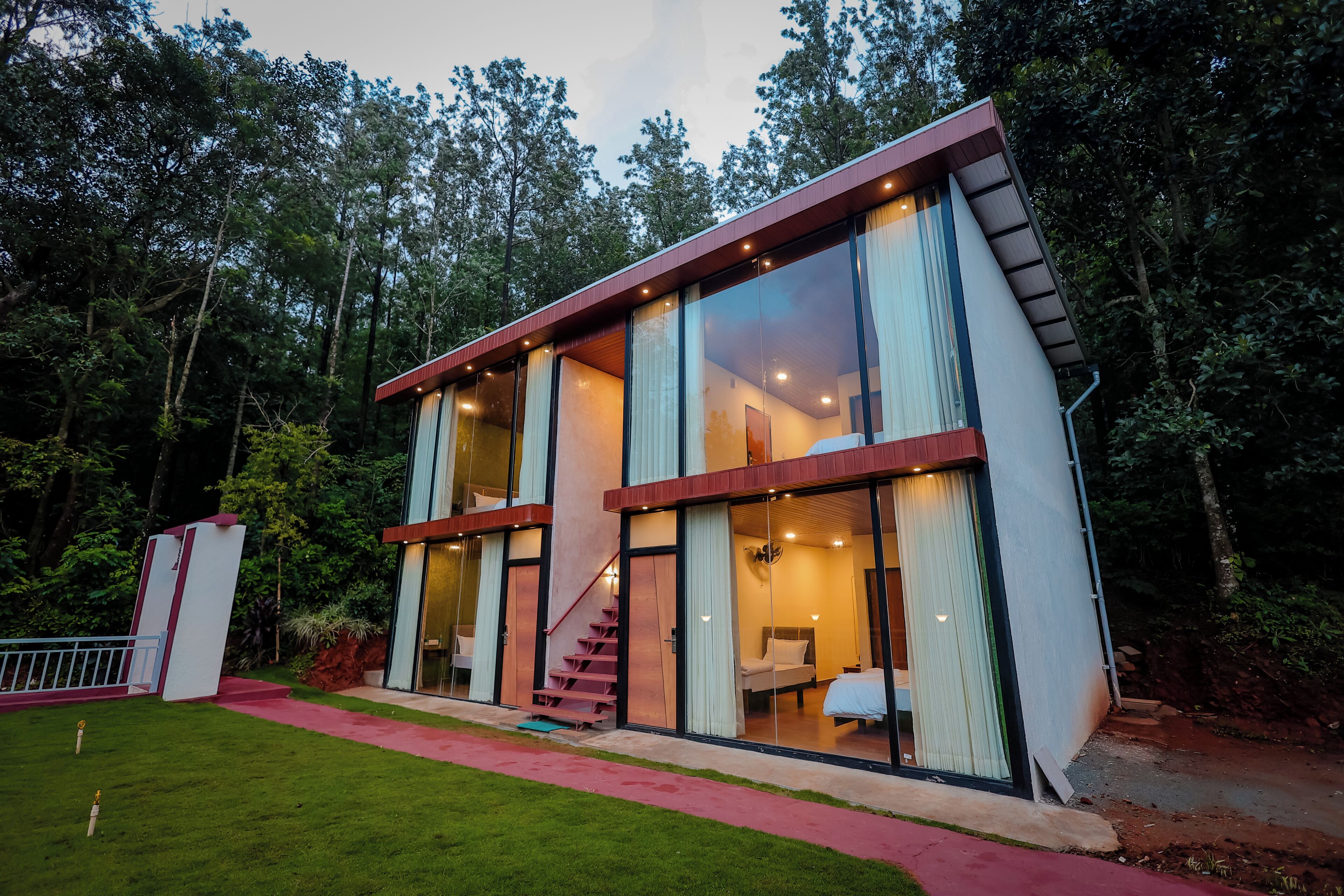 Una casa moderna de dos pisos con amplios ventanales, una escalera y un césped cuidado.