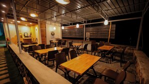 An indoor dining area with multiple tables and chairs, a counter, and a wooden ceiling structure. - Honey Drop by Mantra (Chikkamagaluru)