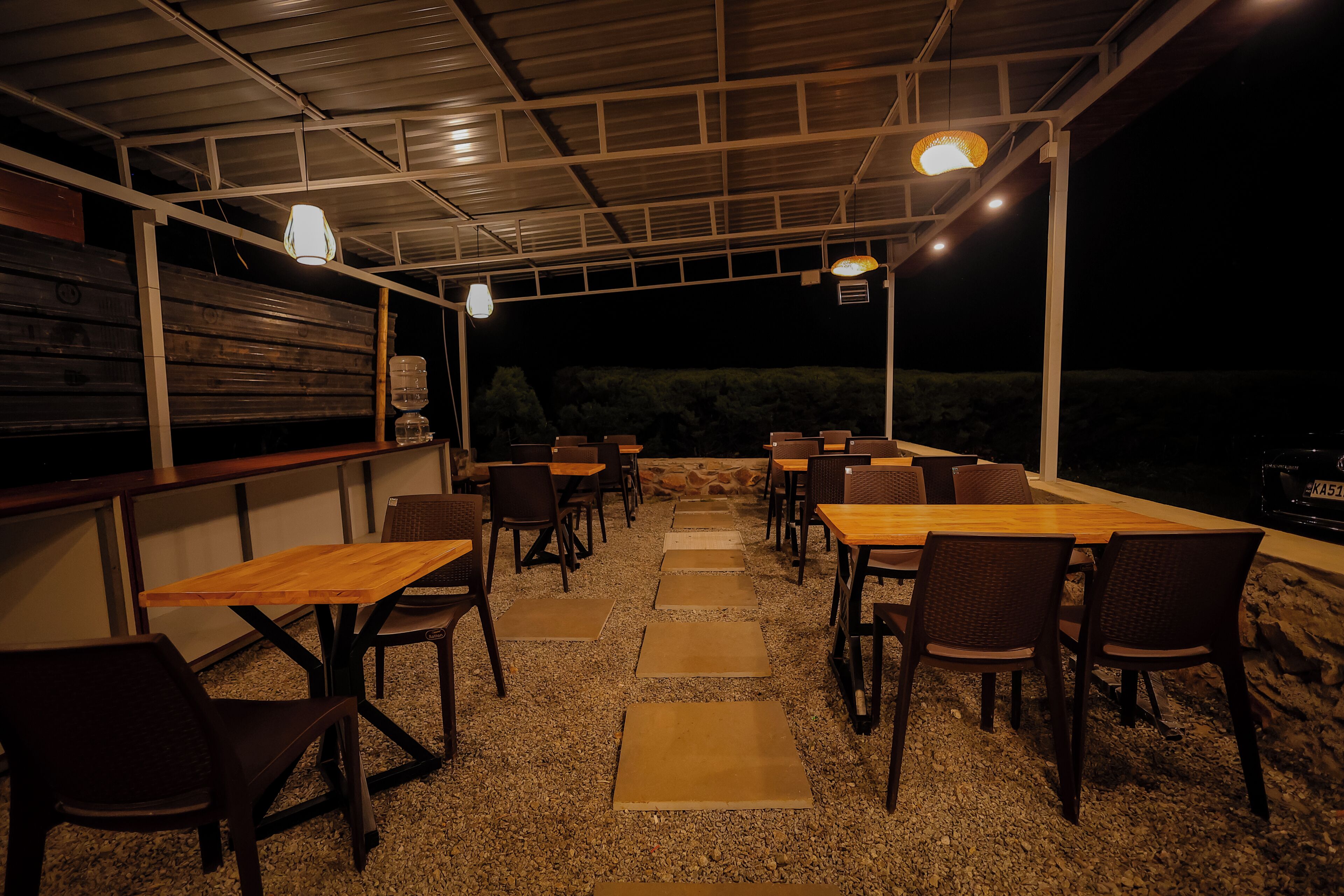Un patio al aire libre con mesas y sillas, un dispensador de agua y vistas al cielo nocturno.