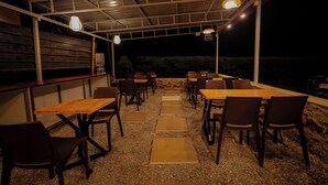 An outdoor patio with tables and chairs, a water dispenser, and a view of the night sky. - Honey Drop by Mantra (Chikkamagaluru)