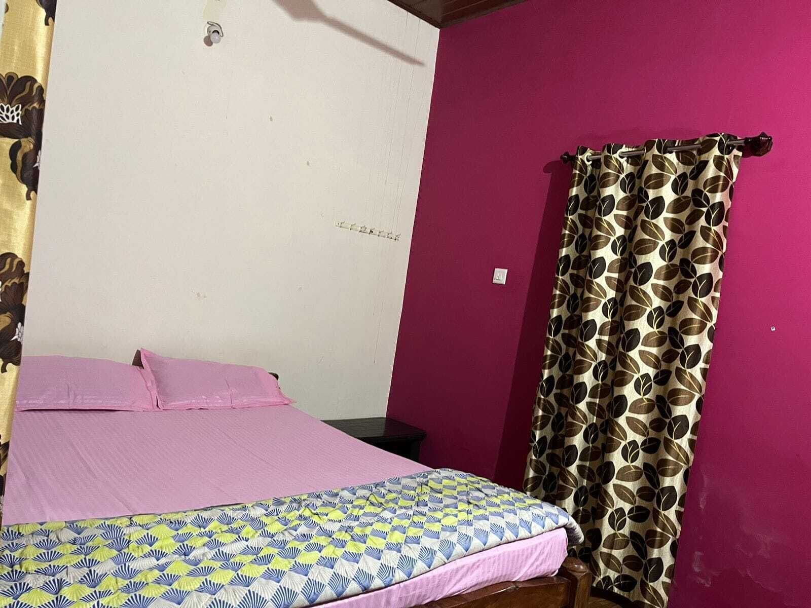 A room with a bed, a curtain, and a wall with a single light switch.