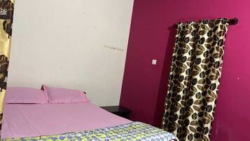 A room with a bed, a curtain, and a wall with a single light switch.
