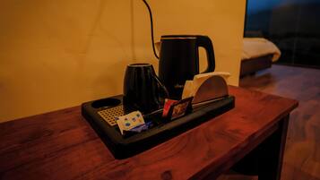 Una habitación de hotel con una mesita de noche de madera, una cafetera negra, una bandeja con un rollo de pañuelos, un paquete de té y un control remoto.