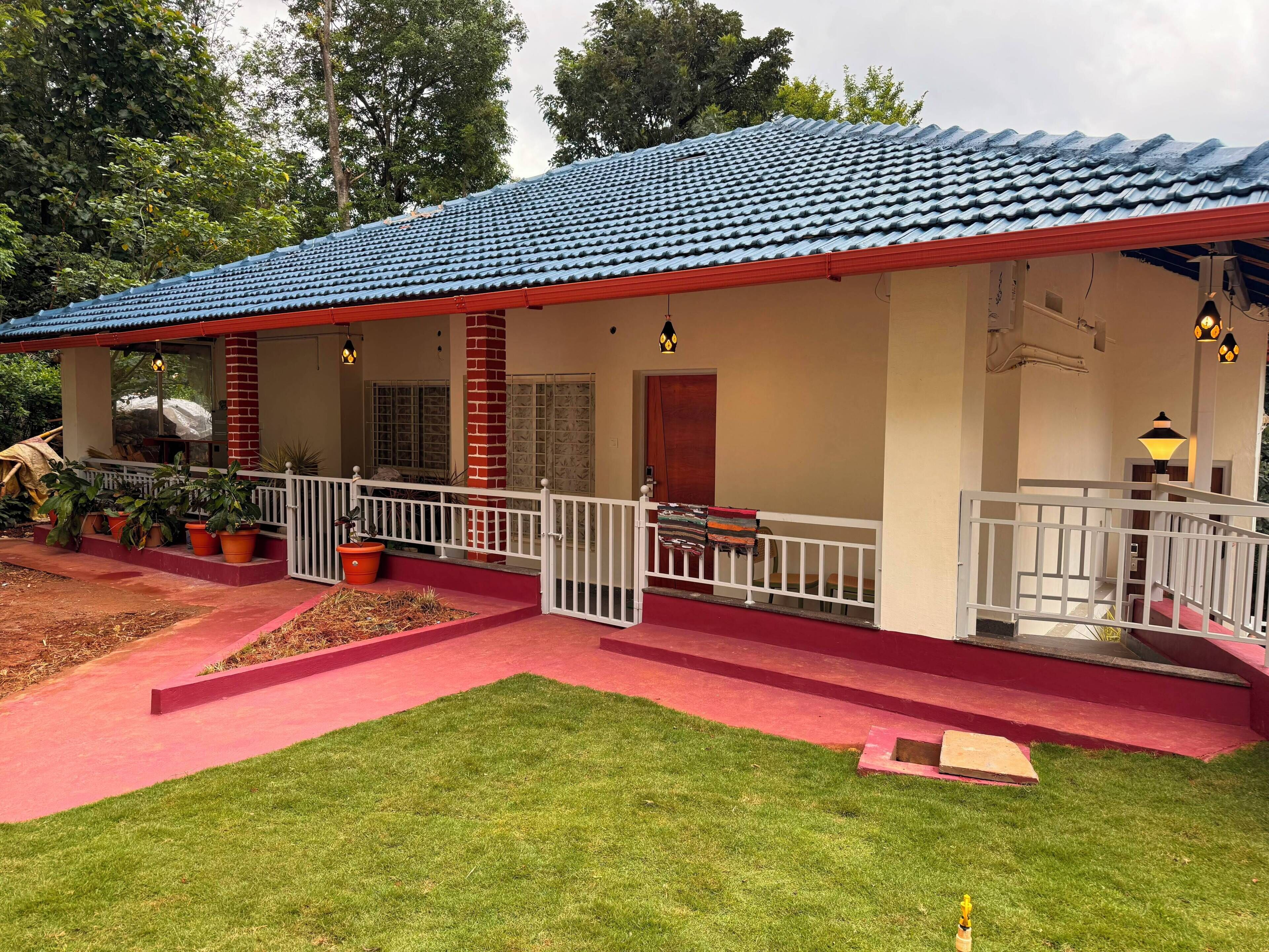 A building with a red and blue tiled roof, a covered porch with a railing, and a small garden area with grass and potted plants.