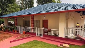 A building with a red and blue tiled roof, a covered porch with a railing, and a small garden area with grass and potted plants.