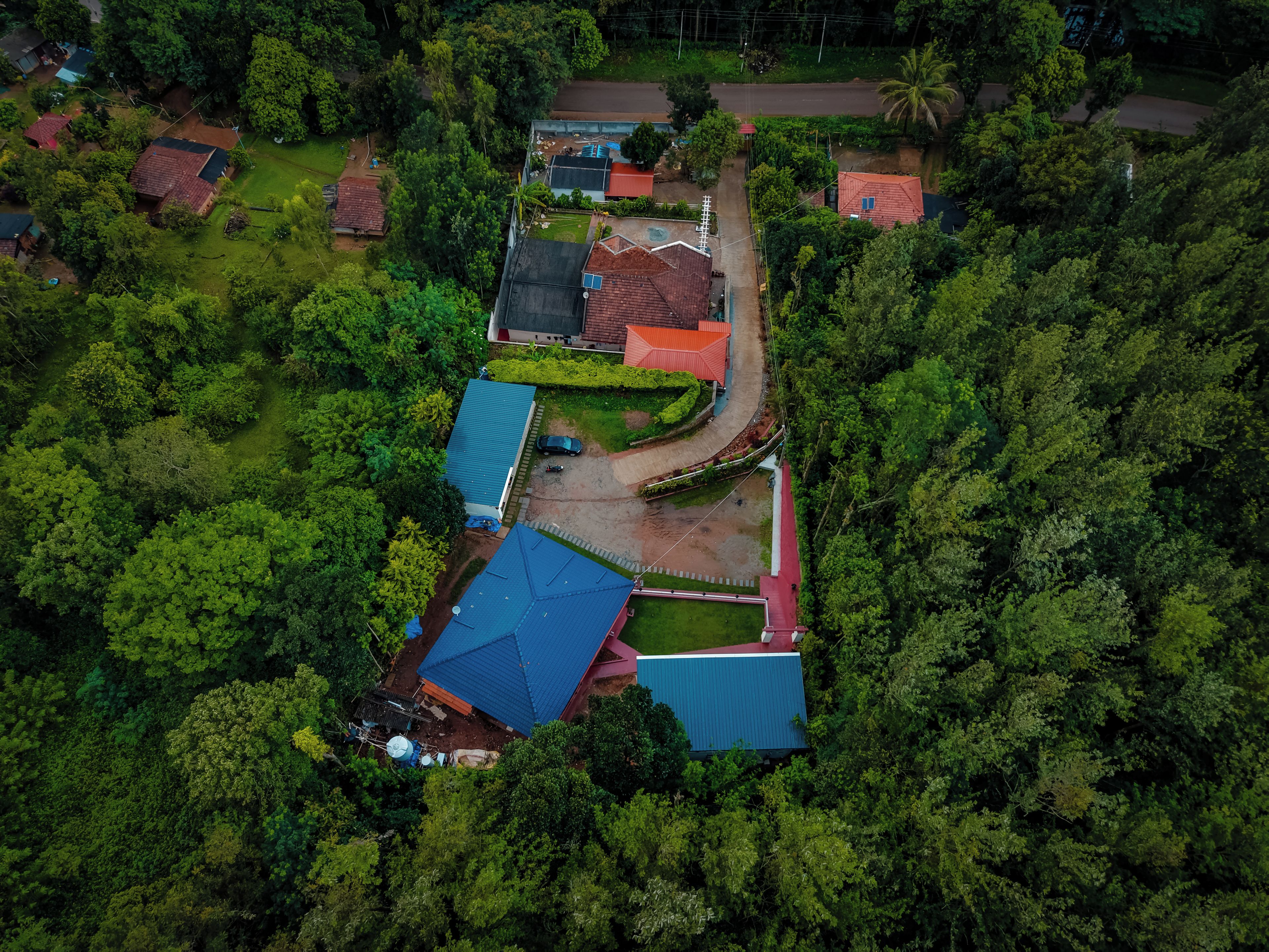 An aerial view of a residential area with multiple houses, surrounded by dense greenery.