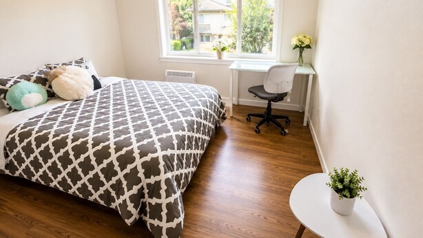 Een slaapkamer met een bed, een bureau, een stoel, een raam en een kleine tafel met een plant.