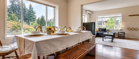 A dining area with a table set for four, large windows, a sofa, and a television.