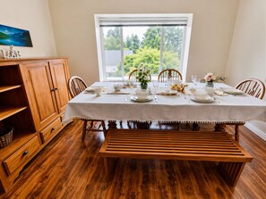 A dining room with a wooden table set for four, a bench, and a view of greenery outside. - Spacious Family House (Seattle)