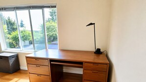 Een houten bureau met lades en een lamp, geplaatst bij een raam met uitzicht op bomen.
