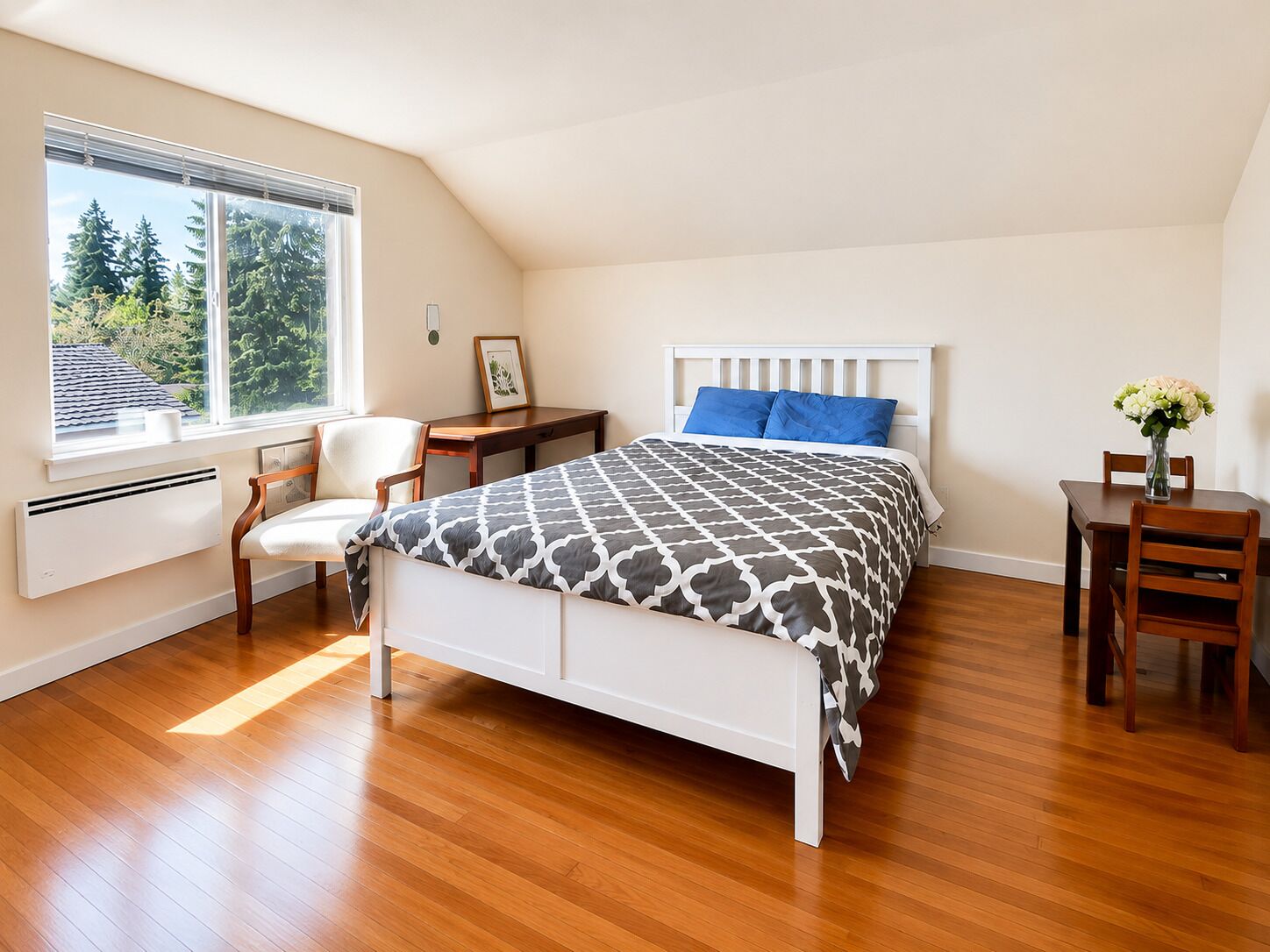 A bedroom with a bed, a desk, a chair, a radiator, and a window with a view of trees.