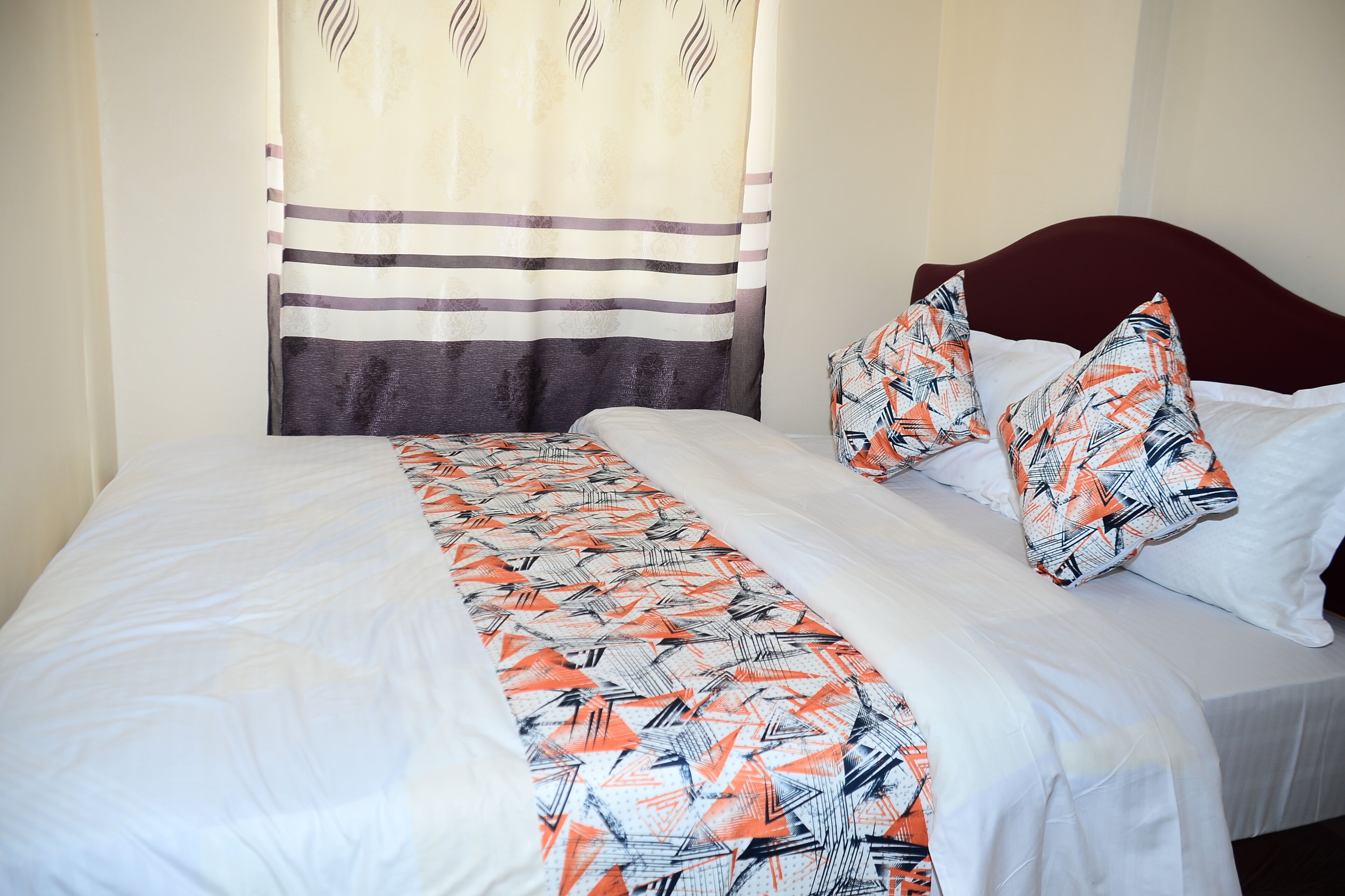 Una cama con una colcha estampada, almohadas y una cortina a rayas.